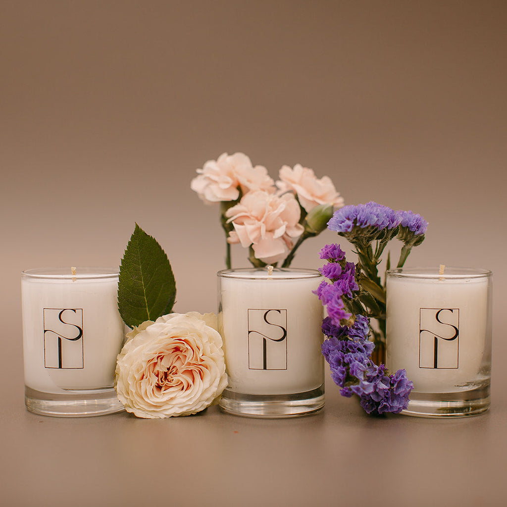 Four candles with floral arrangements and a logo on a brown background