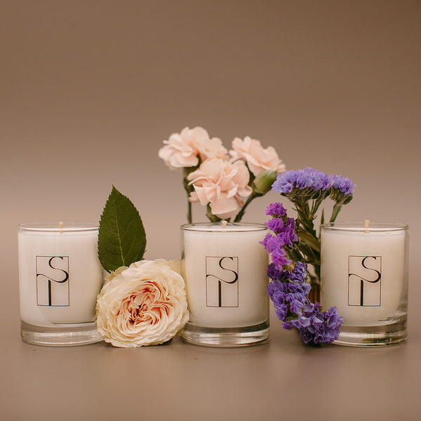 Four candles with floral arrangements and a logo on a brown background