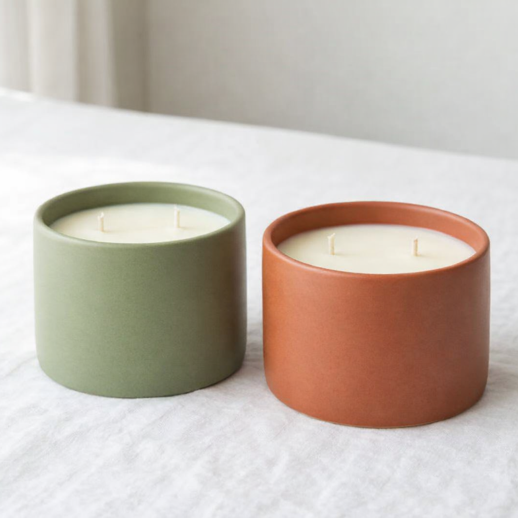 Two candles in ceramic containers on a white surface