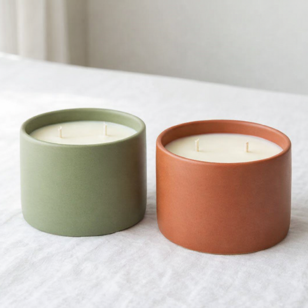 Two candles in ceramic containers on a white surface